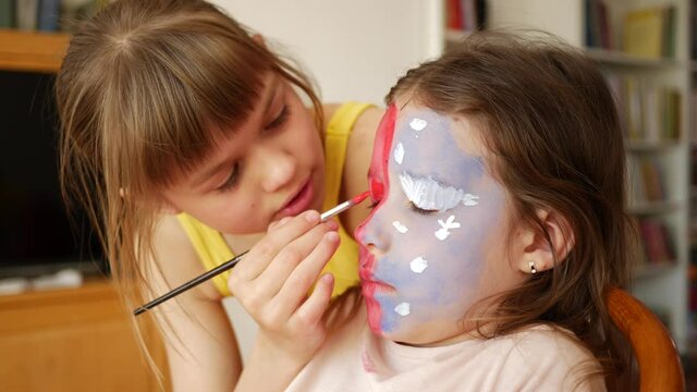 Sisters girls at home. Children painting on face skin making body art to each other with colored paint