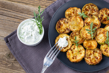 Fried slices of zucchini with sour cream sauce. Courgettes with herb for dinner on natural wooden background