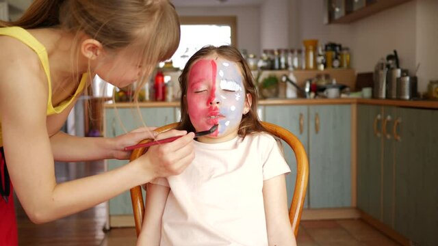 Sisters girls at home. Children painting on face skin making body art to each other with colored paint