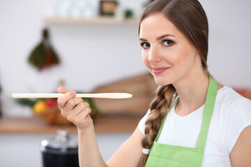 Young woman is cooking in a kitchen. Housewife is tasting the soup by wooden spoon