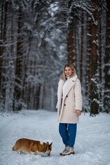 Young blonde female is playing with her welsh corgi pembroke in a winter snowy forest