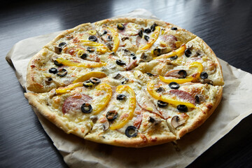 Round pizza with chesse, ham, yellow bell pepper, olives and mushrooms on wooden table