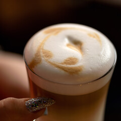 Glass of latte coffee with froth in female hand. Close up shot, top view. Soft focus.