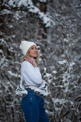 Fototapeta premium Young blond beautiful female with white ice skates in her hand in winter snowy forest.