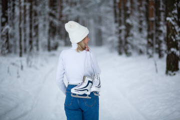 Young blond beautiful female with white ice skates in her hand in winter snowy forest.