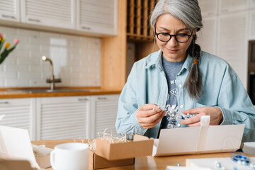 Mature grey woman in eyeglasses while wrapping present at home