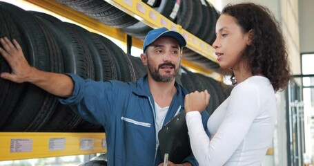Salesman mechanics of tires talking about characteristic of product to customer came to look at assortment represented in auto service shop.