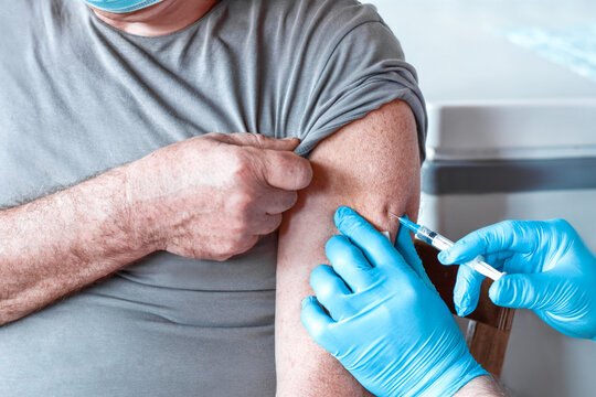 Elderly Man In Face Mask Getting Covid Vaccine. Doctor Giving Injection To Senior Man At Hospital. Virus, COVID-2019, Flu Protection. Vaccination Of Old Patient In Clinic During Coronavirus Pandemic.