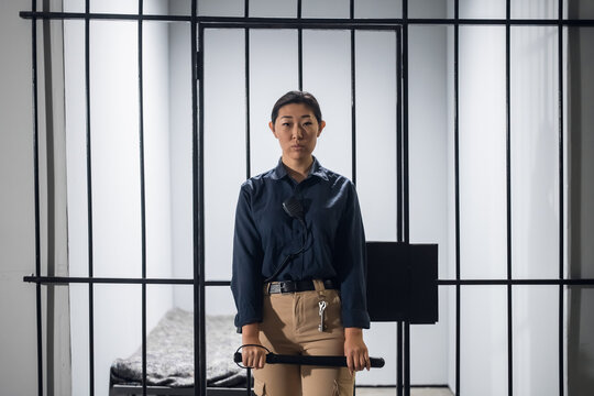 Asian guard in uniform In full armor with a baton and a pistol on the background of a prison cell