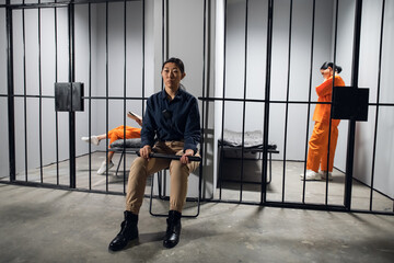 Fototapeta premium A typical day in a women's prison. A bored female guard in uniform sits near the cells with female prisoners.