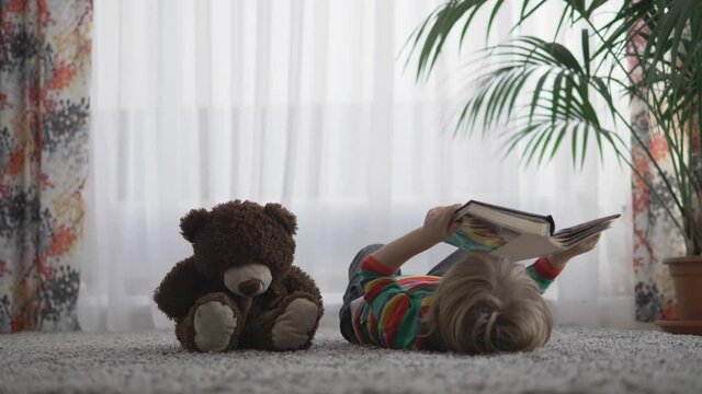 Child lying down on carpet look on photo book, teddy bear toy