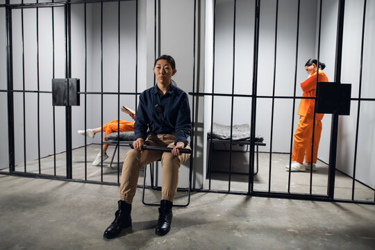 A typical day in a women's prison. A bored female guard in uniform sits near the cells with female prisoners.