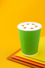 Coffee Cappuccino in a paper green cup on colorful yellow background. Mockup. Cappuccino coffee take away. Space for text. Close up