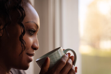 eine Frau steht vor einem Fenster und trinkt Kaffee