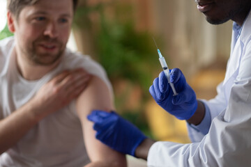African doctor with syringe doing injection of vaccine to male patient