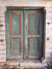 An old wooden door of an abandoned house. In green-brown color. Faded. At a traditional village, near Vikos gorge.