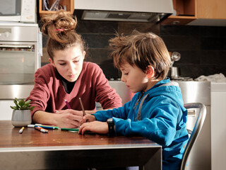 Children draw on sheets of paper with pencils and markers, sitting at the table in the kitchen at home.