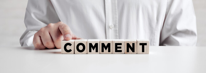 Businessman pressing his finger on the wooden cubes with the word comment.