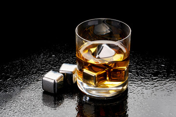 Whiskey with steel cooling cubes on dark glass background