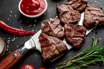 several mini Grilled beef T-bone steaks on the knife on stone background