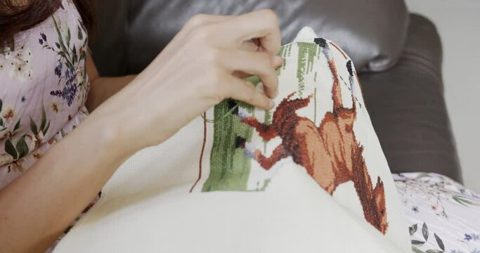 Woman hands doing cross-stitch of picture of a skittish horse at home, close up of embroidery. 
