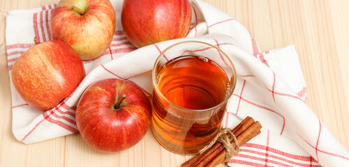 squeezed apple juice in the glass with kitchen towel and apples with cinnamon at the background on the wooden table background