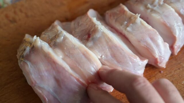Close up shot of slices of monkfish arranged on a cutting board. One hand touches and checks the slices. Mediterranean diet, food and health concept.