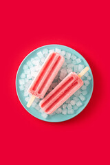 Strawberry popsicles with ice on red background
