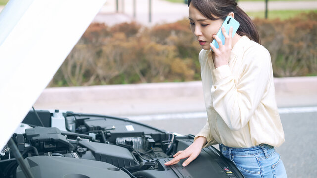 自動車のボンネットを開けてスマホで通話する女性　故障　ロードサービス