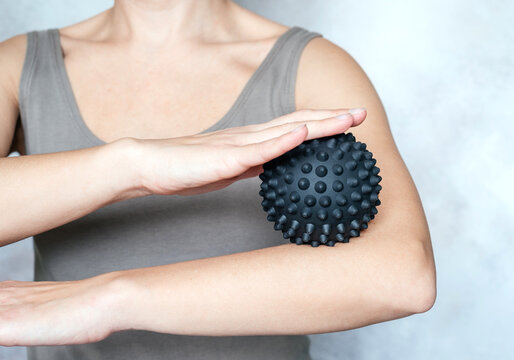 A woman holds a spiky trigger point massage ball used for muscle pain treatment and deep tissue massage