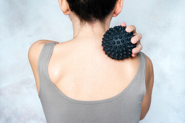Young woman massages her back with spiky trigger point ball, muscle pain treatment reflexology....