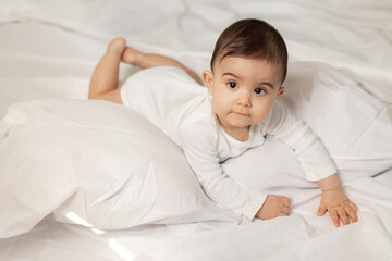 Cute little girl in a white bodysuit lies in bed with cotton linen. High quality photo.