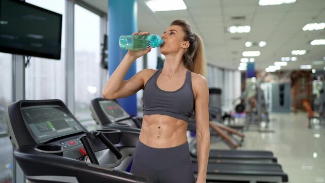 Gym woman working out drinking water standing by fitness machines