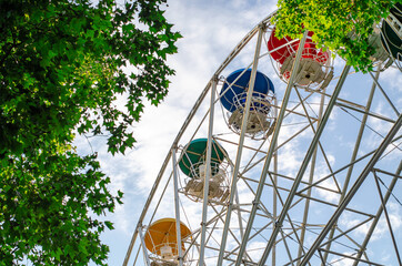 Ferris wheel with multi-colored booths. Green tree