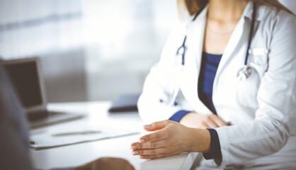 Fototapeta premium Unknown woman-doctor is talking to her patient, while they are sitting together in the cabinet in a clinic. Female physician with a stethoscope at work, close-up. Perfect medical service in a hospital