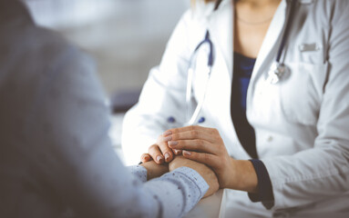 Unknown woman-doctor is holding her patient's hands to reassure the patient, discussing current...