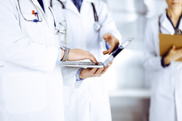 Group of unknown doctors, men and a woman, with stethoscopes, discuss medical exam resoults, using a laptop, while standing at hospital office. Physicians using a laptop for checking up medication