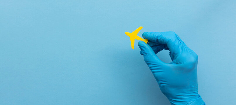 A person wearing a medical surgical glove holding a yellow travel airplane