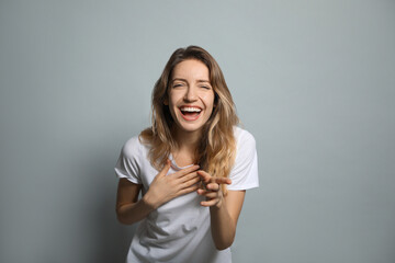 Cheerful young woman laughing on grey background