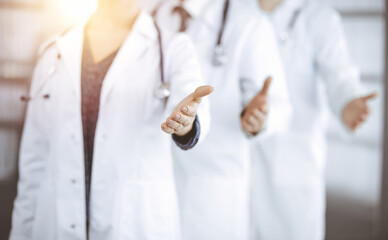 Doctors standing as a team while offering helping hand for shaking hand or saving life in sunny clinic. Medicine concept