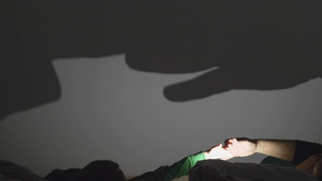 Detail of parent hand making shadows on wall, children look and enjoy imagination play