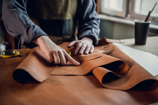 The initial stage of production of leather shoes, a young guy lays out the leather on the table for further use