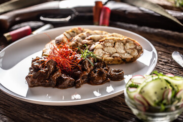 Porcelain plate full of deer venison goulash stew served with dumpling and fresh salad as an...