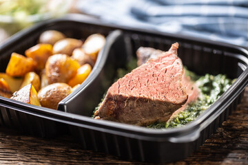 Delicious red meat sous vide steak packed in portable take away plastic box and served with crunchy roasted potatoes and savory spinach dip and fresh vegetable salad