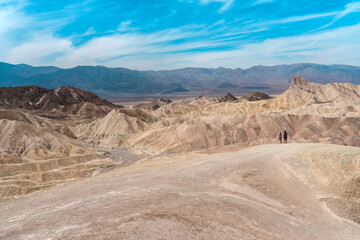Fototapeta na wymiar Amazing view of the hills in Zabriskie Point Death Valley National Park, USA. In the distance, small silhouettes of people