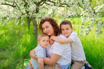 Naklejka na ściany i meble picnic. mother with sons cuddle in flowering garden. mother's day
