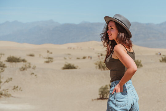 A young woman wearing a hat walks through the hot desert in Death Valley, picturesque Sand Dunes, USA