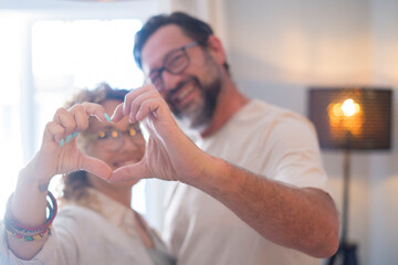 Happy adult couple in love do heart sign with hands - relationship people enjoy home together -...