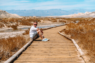 A young man in a white shirt sits on a bridge in Death Valley in the scenic Salt Creek Interpretive Tra