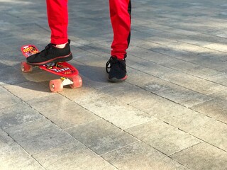 Fragment of the legs of a boy in red sportswear on a skateboard on a city street, active and healthy lifestyle, sports and childhood